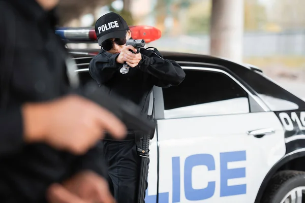 Poliskvinna Solglasögon Med Pistol Nära Kollega Suddig Förgrund Och Bil — Stockfoto