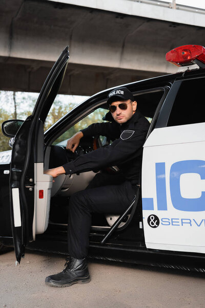 Policeman in sunglasses sitting in car on urban street 