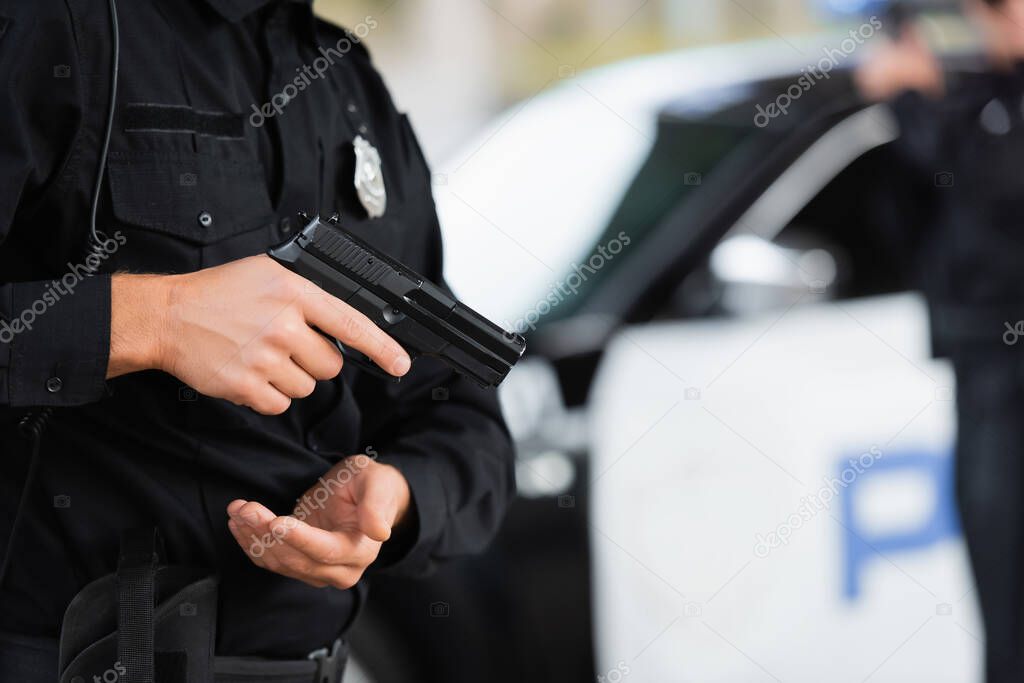 Cropped view of policeman holding firearm near car on blurred background outdoors 