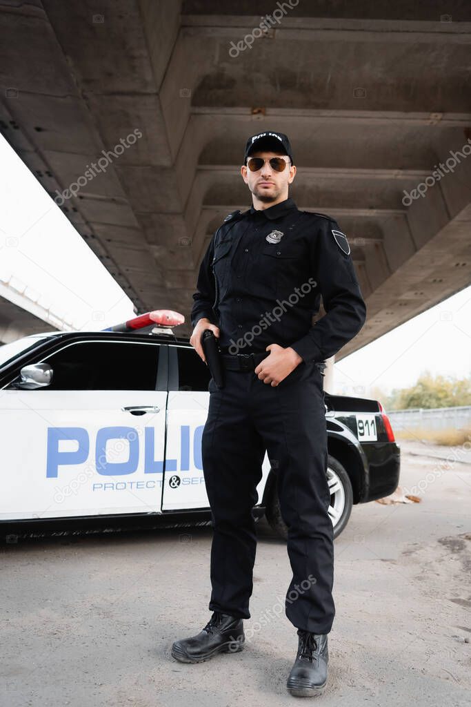 Officer of police holding gun near car on urban street 