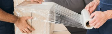 cropped view of movers wrapping box with stretch film, banner clipart