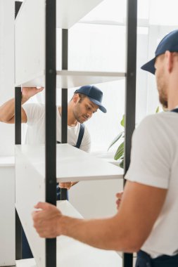 Hintli nakliyeci ön planda iş arkadaşıyla ağır askılar taşıyor. 