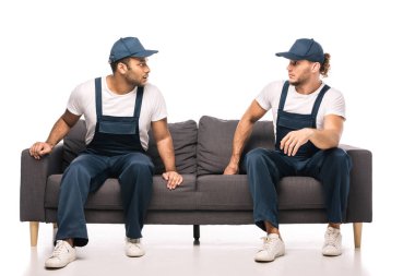 Tam boy şok olmuş çok kültürlü nakliyeciler beyaz kanepede otururken birbirlerine bakıyorlar. 