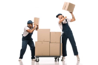 Üniformalı kızgın bir nakliyeci, korkmuş Hintli iş arkadaşının yanında karton kutu ve beyaz paketler taşıyan el arabası tutuyor.