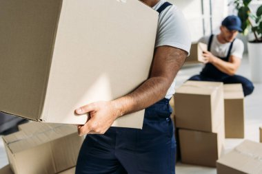 cropped view of indian mover holding carton box near coworker on blurred background clipart