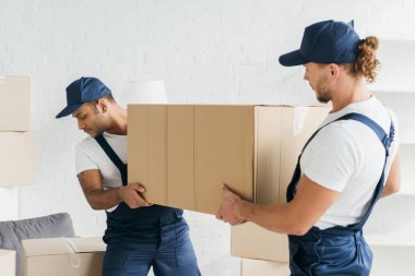 Üniformalı çok ırklı nakliyeciler büyük bir kutu taşıyorlar. 