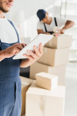Hindistan 'daki iş arkadaşının yanında elinde dijital tablet bulunan üniformalı işçilerin bulanık arka planda paketleme kutuları var. 
