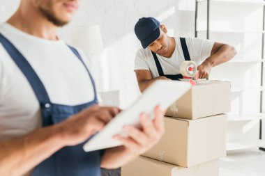 Bulanık ön planda dijital tablet tutan iş arkadaşının yanındaki Hintli nakliyeci paketleme kutusu 
