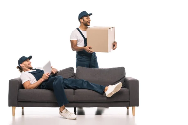 快乐的劳动者躺在沙发上 带着数码平板电脑 接近快乐的印第安人搬运工 手里拿着白色的盒子 — 图库照片