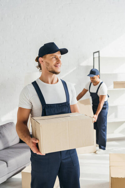 young worker in uniform holding carton box near indian coworker 