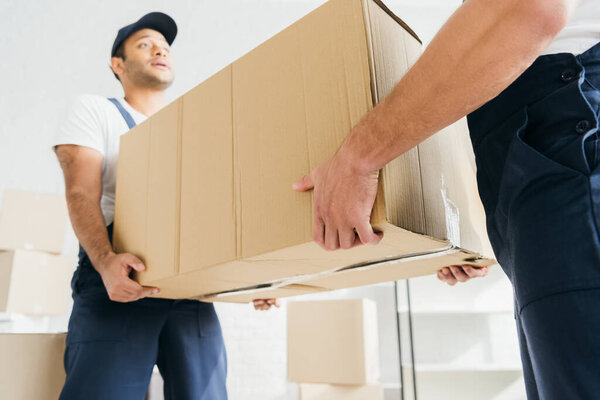 low angle view of multiethnic movers in uniform carrying huge carton box 