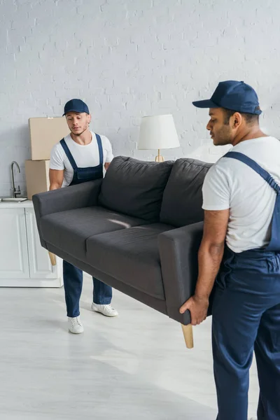 Jóvenes Multiétnicos Con Gorras Uniforme Llevando Sofá Apartamento — Foto de Stock