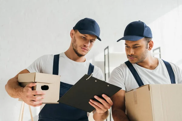Multicultural Movers Holding Boxes Looking Clipboard Apartment — Stock Photo, Image