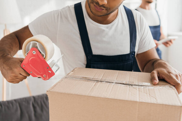 cropped view of indian mover in uniform packing box in apartment 