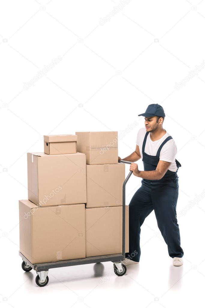 full length of indian mover in overalls pulling heavy hand truck with carton boxes on white