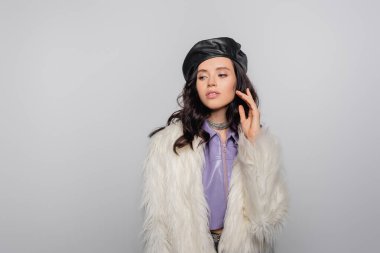 brunette young woman in stylish white faux fur jacket and leather beret posing on grey background clipart
