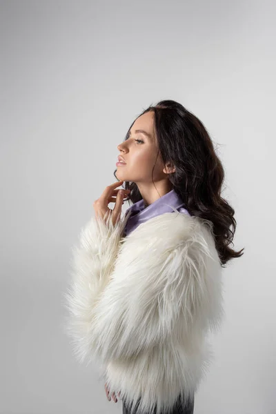 ブルネット若いです女性でスタイリッシュなホワイトフェイクファージャケットPosing上の灰色の背景 — ストック写真