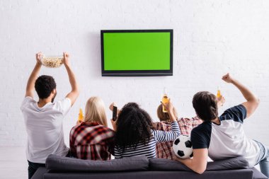 Çok kültürlü futbol hayranlarının televizyonda şampiyonluk maçı izlemesi ve kazanan jestler göstermesi.