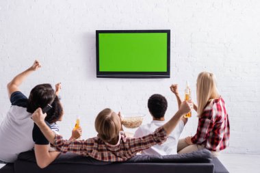 Heyecanlı çok kültürlü sporseverler televizyonda şampiyonluk maçı izlerken zafer jesti gösteriyorlar.