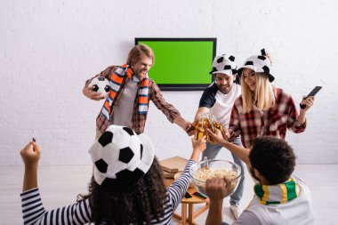 Futbol fanatikleri içinde neşeli çoklu etnik arkadaşlar. Duvardaki LCD TV 'nin yanında bir şişe bira tokuşturuyorlar.
