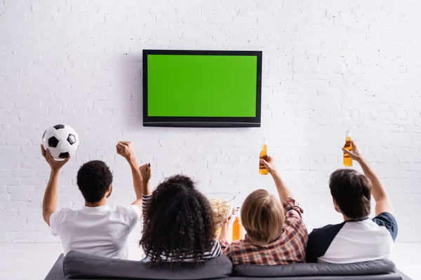 back view of multicultural football fans showing win gesture while watching championship on tv