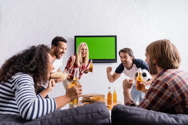 興奮したサッカーファンがビールを持ち壁にLcdテレビの近くで勝者のジェスチャーを示す — ストック写真