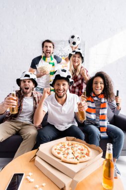 Heyecanlı adam çok ırklı arkadaşlarıyla futbol şampiyonasını izlerken zafer jesti yapıyor.