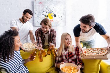 heyecan dolu çoklu etnik arkadaşlar evde parti yaparken bira, pizza ve atıştırmalıklar tutuyorlar.