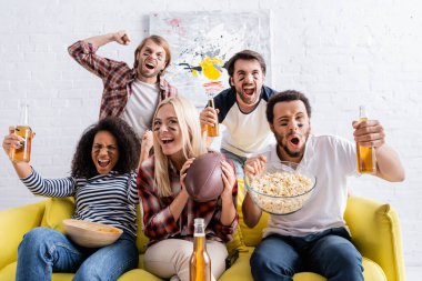 excited multiethnic friends with painted faces holding beer and shouting while watching rugby championship  clipart