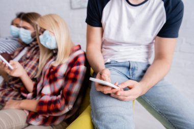Tıbbi maskeli çok ırklı arkadaşlar bulanık arka planda cep telefonlarıyla sohbet ediyorlar.
