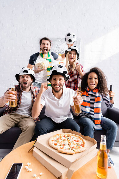 excited man showing win gesture while watching football championship with multiethnic friends