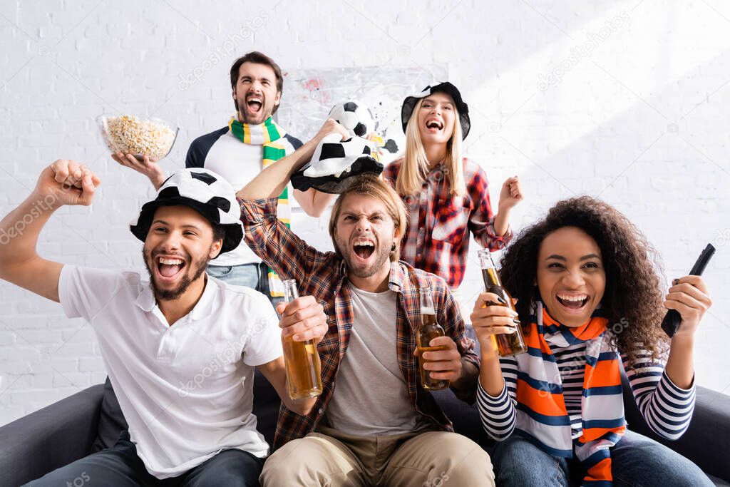 excited multiethnic friends showing win gesture while watching football championship at home
