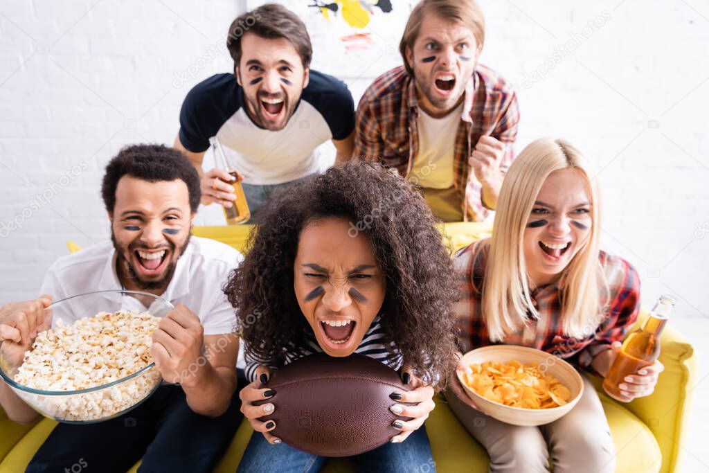 excited multiethnic sports fans with painted faces screaming while watching american football championship 