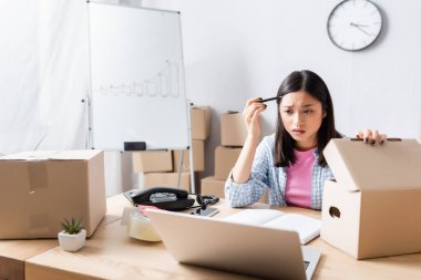 Kalemle yardım merkezindeki karton kutuyu açıp laptopa bakan Asyalı bir gönüllü.