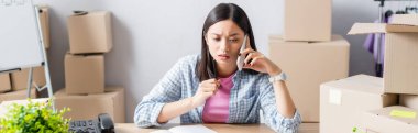 Asyalı ciddi bir gönüllü, yardım merkezinde, pankarton kutuların yanında akıllı telefondan konuşuyor.