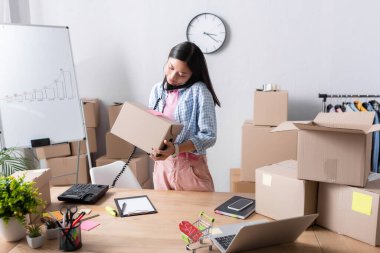 Yardım merkezinde karton kutuların yanında dururken telefonda konuşan paketli bir Asyalı gönüllü.