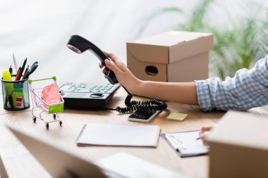 Fiyat etiketi, dizüstü bilgisayarı ve ön planda bulanık kutuları olan oyuncak alışveriş arabasının yanında telefon tutan gönüllülerin görüntüsü. 