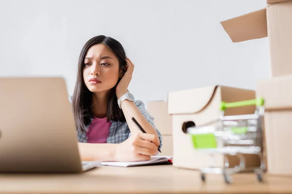 Serious Asian Volunteer Looking Laptop While Writing Notebook Carton Boxes — Stock Photo, Image