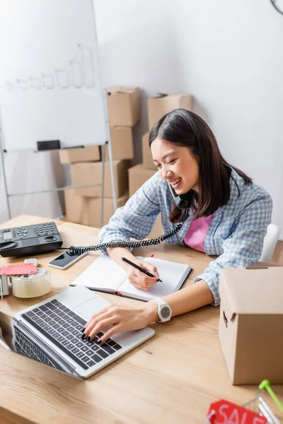 Glimlachende Aziatische Vrijwilliger Met Pen Telefonisch Pratend Laptop Aan Bureau — Stockfoto