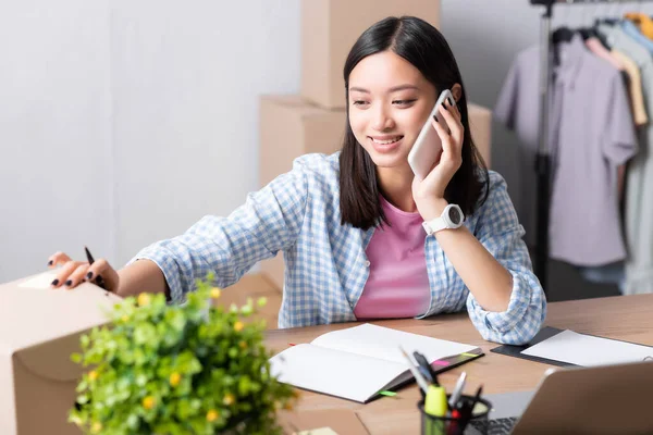 Smiling Asian Volunteer Talking Smartphone While Opening Carton Box Desk — Stok Foto