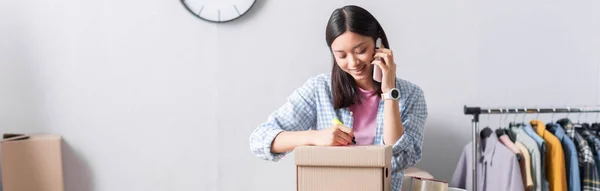 Lächelnder Asiatischer Freiwilliger Spricht Auf Smartphone Und Schreibt Auf Karton — Stockfoto