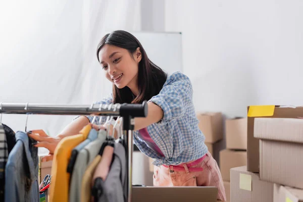 Smiling Asian Volunteer Looking Clothes Hanging Rack Burred Foreground Charity — Stock Photo, Image