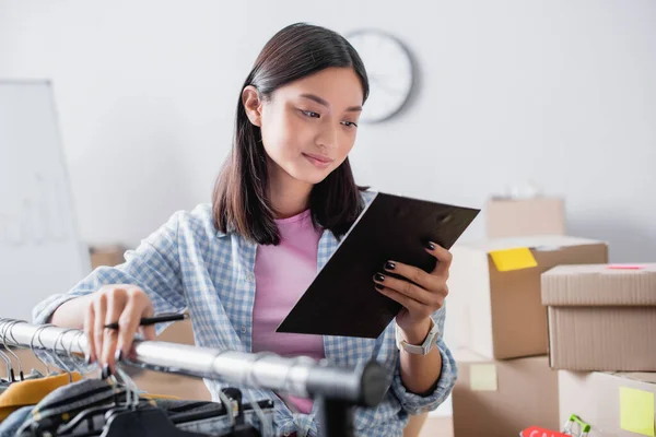 Asiatisk Volontär Hålla Penna Och Titta Urklipp Nära Kläder Hängande — Stockfoto