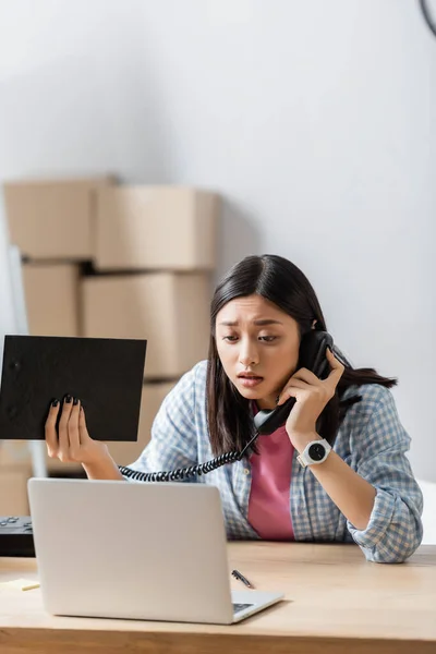 Worried Asian Volunteer Talking Telephone While Holding Clipboard Laptop Blurred — Stock Photo, Image