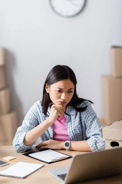 Pensive Asian Volunteer Holding Pen Looking Laptop Box Clipboard Blurred — Stock Photo, Image