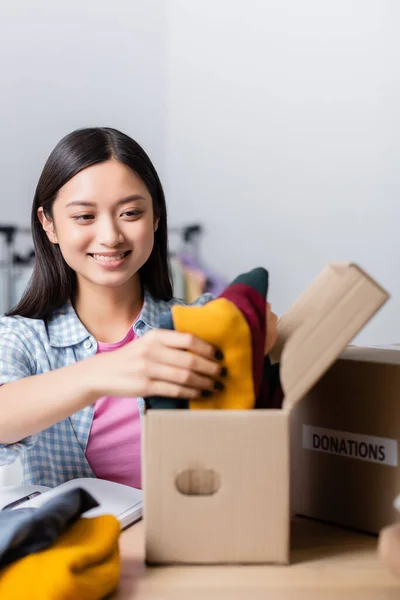 Glada Asiatiska Volontär Packning Kläder Rutan Nära Anteckningsbok Bordet Välgörenhet — Stockfoto