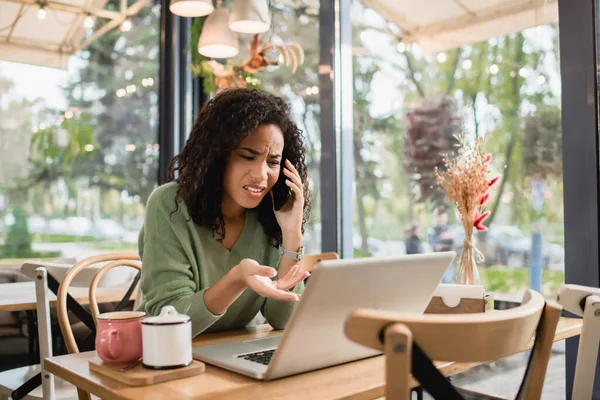 Displeased African American Woman Talking Smartphone Pointing Hand Laptop Cafe — Stock Photo, Image