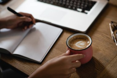 Not defterine yazarken elinde latte olan Afro-Amerikan kadın manzarası. 