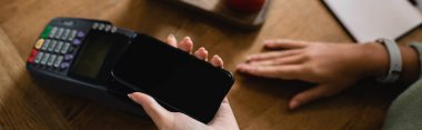 Afro-Amerikalı bir kadının kafeteryada, afişte akıllı telefonla ödeme yaptığı görüntüler.