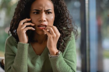 Kafede akıllı telefondan konuşan endişeli Afrikalı Amerikalı kadın.